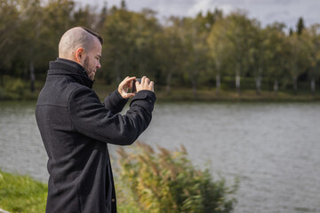 A man takes a picture at a small lake with his mobile phone