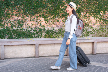Smiling woman traveller dragging black suitcase luggage bag walking to passenger boarding in airport, Travel concept