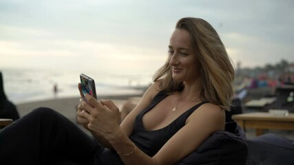 Young woman texting on smartphone sitting at beach bar - Powered by Adobe