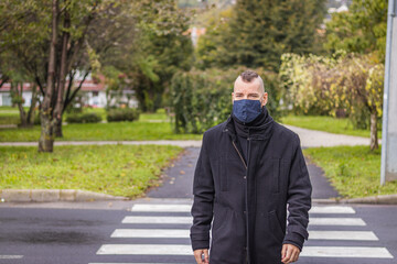 A man walks in the dripping rain while wearing a mask in a small city in Hungary