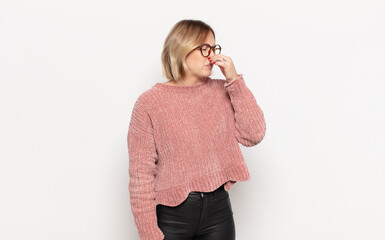 young pretty woman feeling disgusted, holding nose to avoid smelling a foul and unpleasant stench