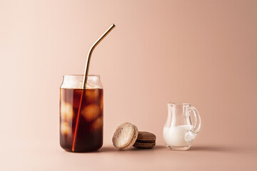 Glass of iced coffee in tall glass with golden straw with cream and macaroons chocolate, vanilla on pastel background for your design. Food concept in vintage style. Copy space. Closeup.