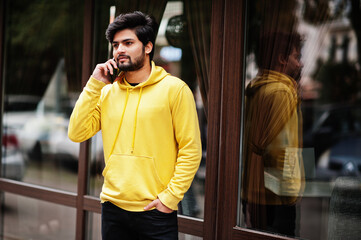 Urban young hipster indian man in a fashionable yellow sweatshirt. Cool south asian guy wear hoodie...