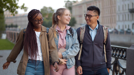 Diverse happy students walking outdoors and chatting during break