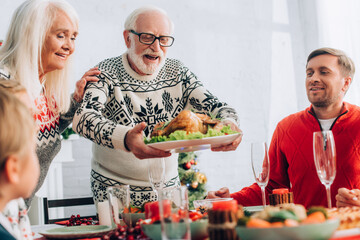 Selective focus of senior man standing near wife, serving turkey on table