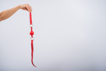Close-up of female hands holding red bdsm gag on white background