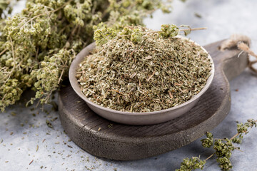 Bowl of dried oregano leaves on stone background.