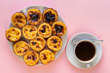 Plate of Pasteis de Belem (aslo called Portuguese Egg Tarts or Pastel de Nata) on a pink background beside a cup of coffee, Food Flat Lay