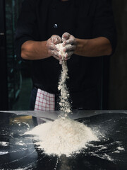 Low light hand chef man with splash of white flour on dark black  background with copy space. An...