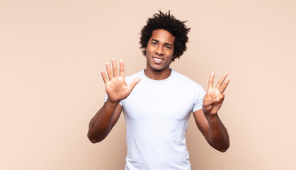 young black afro man smiling and looking friendly, showing number nine or ninth with hand forward,...