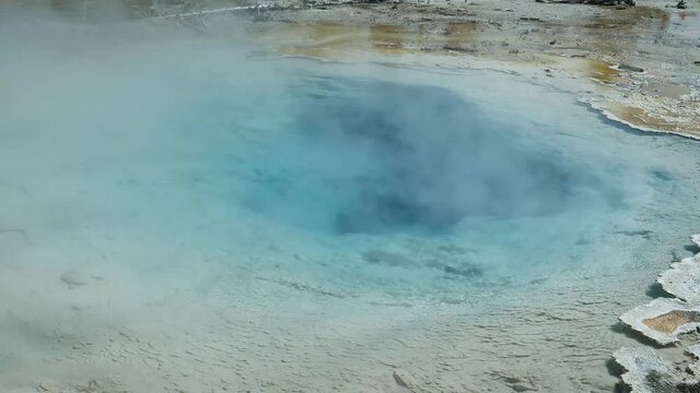 Steam rises from the clear turquois hot water of the geothermal Silex Spring in Yellowstone National Park's Lower Geyser Basin