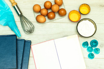 Open blank recipe book, eggs and flour on wood table