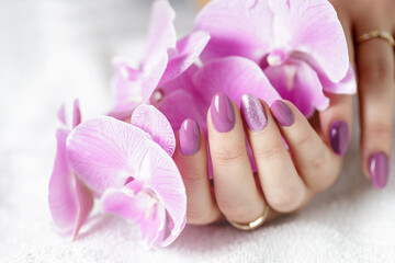 Elegant female hands with fresh pink lilac manicure with orchid flower