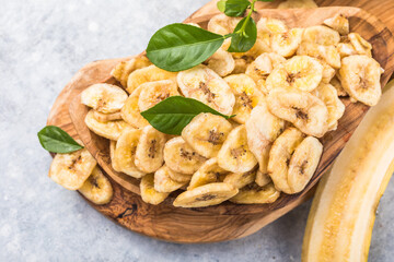 Homemade Dehydrated Banana Chips in a Bowl and fresh banana and slices on table