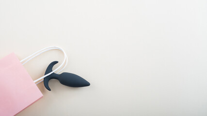 Top view of a black butt plug in a paper bag on a white background. Shopping in a sex shop