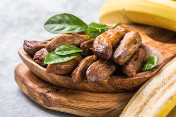 Sun dried bananas in wooden bowl on stone background. Copy space. Superfood, vegan, vegetarian concept.