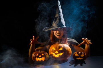 The evil witch casts a spell on pumpkins. Portrait of a woman in a carnival halloween costume in...