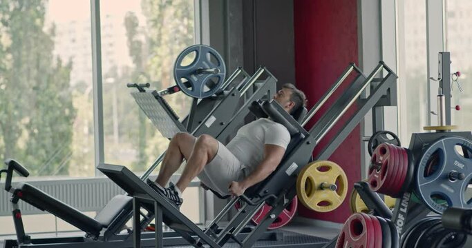 Hard bodybuilding workout. Concentrated man exercising on squat training machine at gym