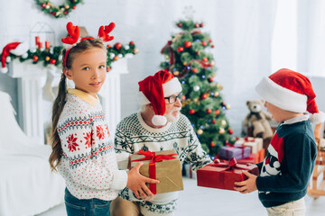 senior man in santa hat taking presents from grandchildren on christmas