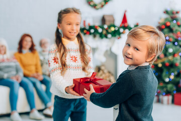 Obraz premium smiling boy looking at camera while presenting christmas gift to happy sister