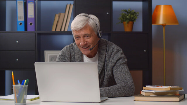 Retired man in headset working as freelancer in internet from home office.