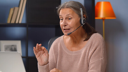 Active senior woman in headset working from home on laptop