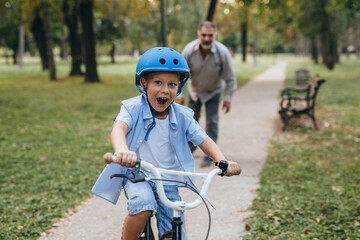 Fototapeta na wymiar boy riding bike in city park with his grandfather