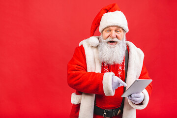 Santa Claus standing isolated on red background. Christmas and new year concept. Using tablet computer.