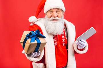 Naklejka premium Santa Claus standing isolated on red background. Christmas and new year concept. Using tablet computer.