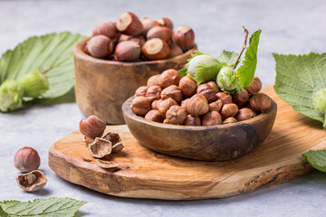 Hazelnuts with peeled hazelnut and leaf  in brown bowl on concrete background.