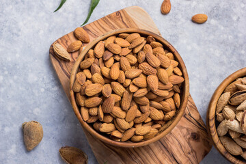 Peeled whole almonds and unshelled almonds in bowl with leaf