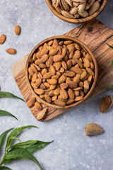 Peeled whole almonds and unshelled almonds in bowl with leaf