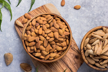 Peeled whole almonds and unshelled almonds in bowl with leaf