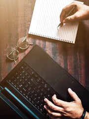 person typing on laptop and writing in notebook or man working on laptop or script