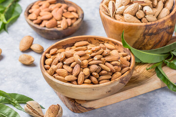 Peeled whole almonds and unshelled almonds in bowl with leaf