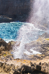 Geyser d'eau sortant d'un trou dans la caye sur le littoral avec la mer bleu intense sur fond de falaise rocheuse