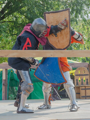 Two foot warriors in heavy medieval armor fight in the arena. Armed with swords. They are protected...