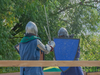 Two foot warriors in heavy medieval armor fight in the arena. Armed with swords. They are protected...