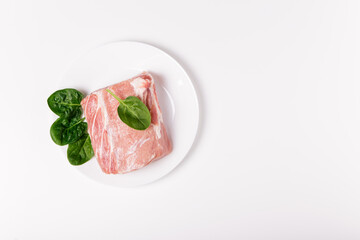 Piece of raw pork meat with spinach on a white ceramic plate. Whole piece of meat on white background. Flat lay, top view, copy space