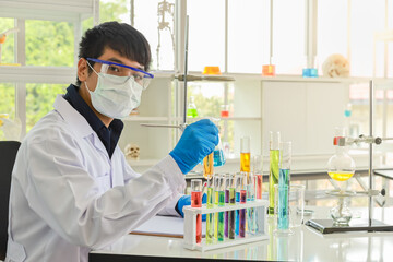 Portrait of young asian professional doctor scientist wearing face mask, glasses and blue rubber gloves holding chemical test tube with glassware to chemical research in working laboratory.