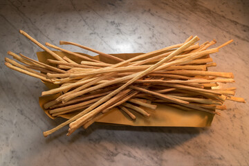 Breadsticks stretched on bread paper, typical crunchy Turin baked grissini on a Carrara marble surface