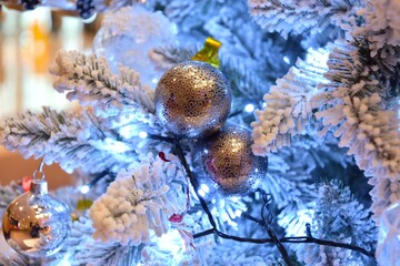 Obraz na płótnie Canvas Christmas tree decorated with silver decorative balls with burning garland and blurred golden background. Defocused christmas background. Christimas tree, decoration and lights. Happy New Year and Xma