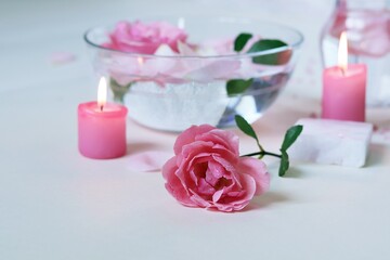 Obraz na płótnie Canvas Fresh pink roses, water, petals, candles on a light background, body care products, natural home cosmetics, healthy lifestyle, alternative medicine