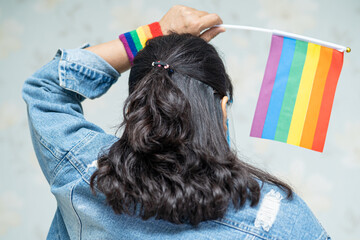 Asian lady wearing mask and face shield for protect covid-19 virus holding rainbow flag, symbol of...