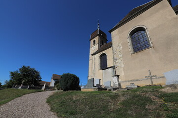 Fototapeta na wymiar Beautiful characteristic small cemetery next to a village church in France. Photo is taken on a warm summer with a blue sky.