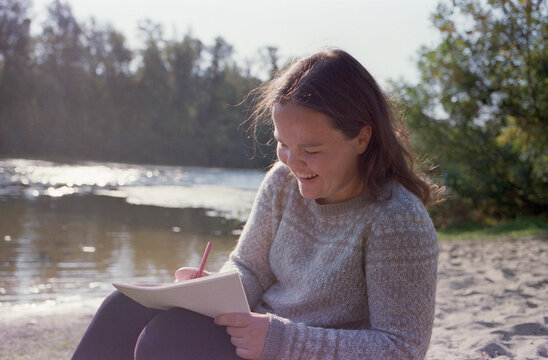 Diabetic woman writes on paper while sitting near the river.