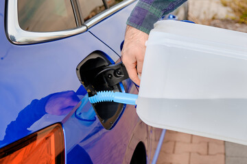 Close up man filling a diesel engine fluid from canister into the tank of blue car. Diesel exhaust...