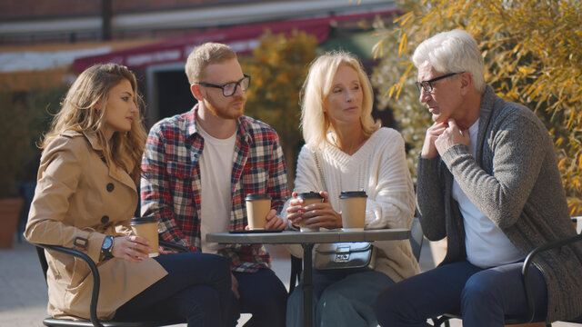 Senior couple and grownup children sitting in outdoors cafe and drinking coffee