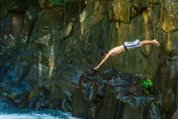 Homme en maillot de bain plongeant dans le bassin d'une cascade entourée de falaises rocheuses...