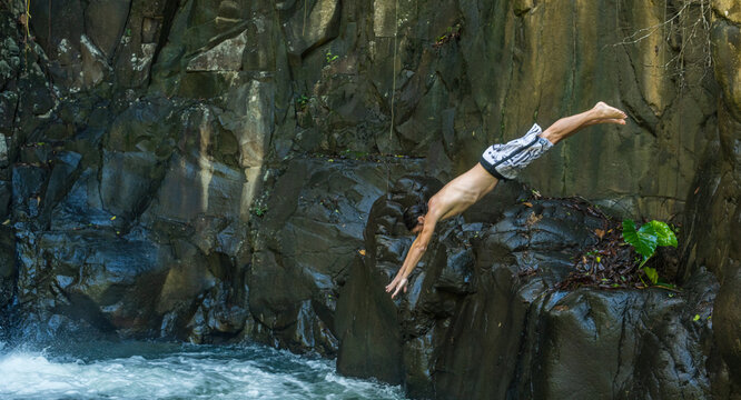 Homme en maillot de bain plongeant dans le bassin d'une cascade entour&eacute;e de falaises rocheuses sombres